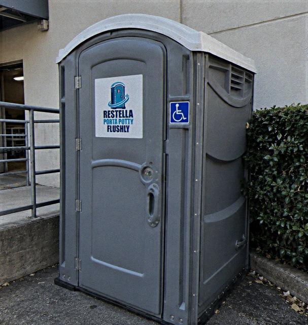 Grey wheelchair accessible portable restroom with a blue accessibility symbol on the side