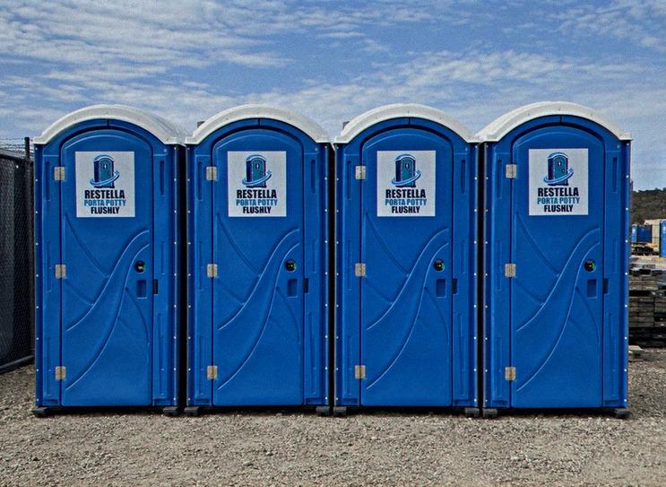 A row of four clean blue portable restrooms set up side by side on a job site
