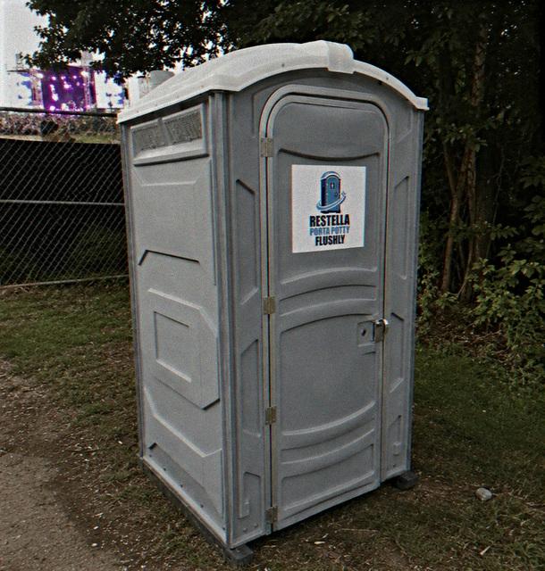 Light grey portable restroom unit set up on grass at an outdoor event