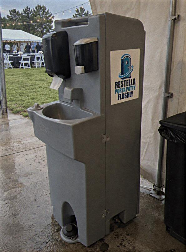 Portable hand washing station standing at the edge of an event tent on a wet day