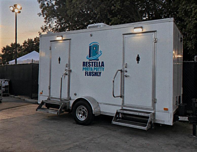 White two-door luxury restroom trailer with steps, set up beside an event area at dusk