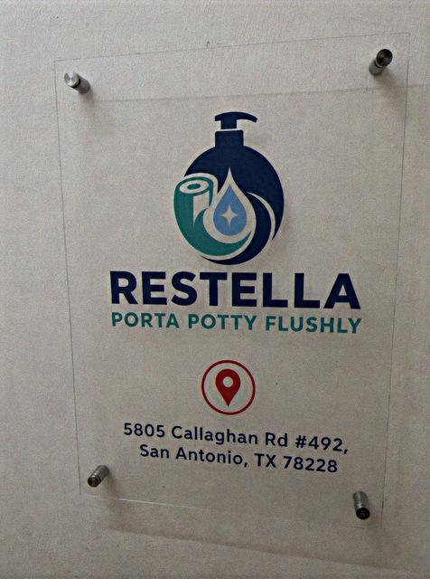Acrylic wall sign reading Restella Porta Potty Flushly with the address 5805 Callaghan Rd #492, San Antonio, TX 78228